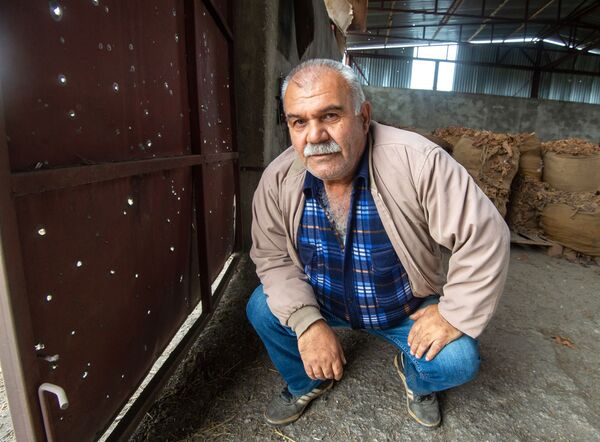 Мужчина у ворот, поврежденных в результате обстрела общины Иванян Нагорного Карабаха - Sputnik Тоҷикистон
