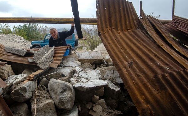 Мужчина у хозяйственной постройки, разрушенной в результате обстрела общины Иванян Нагорного Карабаха - Sputnik Тоҷикистон