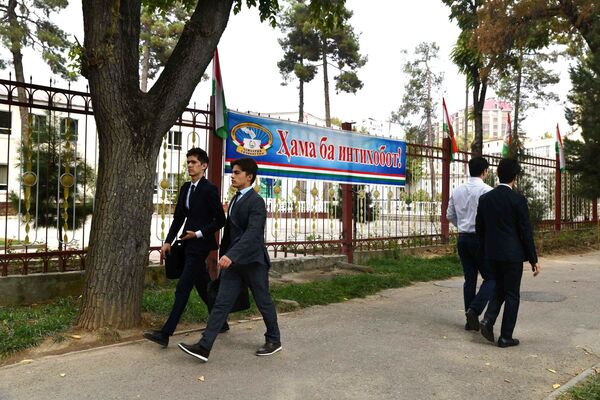 Молодые люди идут по улице Душанбе мимо плаката Все на выборы! - Sputnik Таджикистан