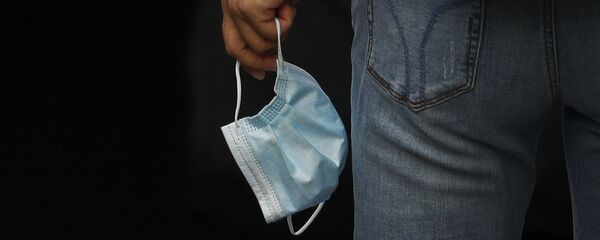 Человек держит защитную медицинскую маску в руке - Sputnik Тоҷикистон