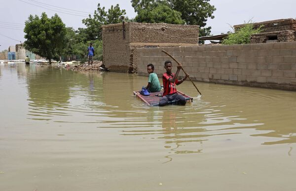Подростки плывут на плоту по затопленной в результате наводнения улице в городе Салмания, Судан - Sputnik Тоҷикистон