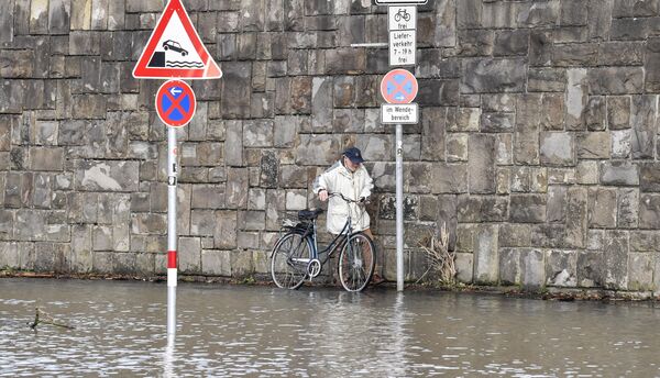 Мужчина толкает велосипед на затопленной набережной в старом городе Дюссельдорфа - Sputnik Таджикистан