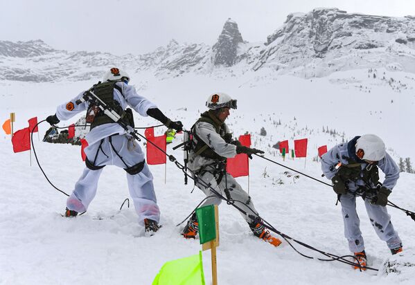 Участники этапа конкурса полевой выучки горных подразделений в зимних условиях поднимают пострадавшего вверх на крутом склоне  - Sputnik Таджикистан