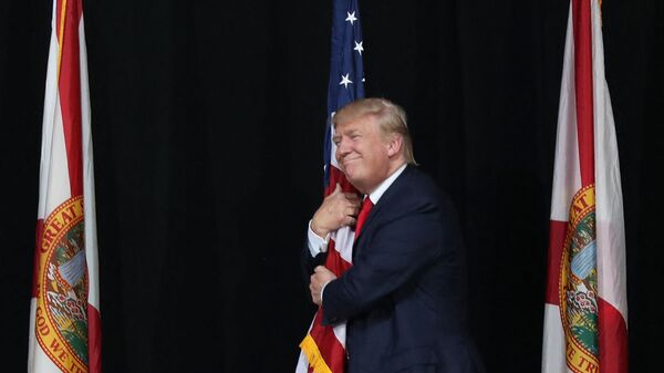 Тампа, Флорида - 24 октября: Кандидат в президенты от республиканцев Дональд Трамп обнимает американский флаг, когда он прибывает на митинг кампании в амфитеатре кредитного союза MidFlorida 24 октября 2016 года в Тампе, Флорида. До президентских выборов осталось 14 дней. Джо Рэдл / Getty Images / AFP (Фото Джо Рэдла - Sputnik Таджикистан