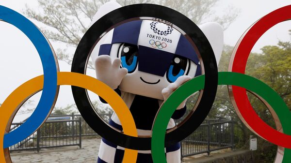 Талисман Летней Олимпиады в Токио Miraitowa позирует сзади Олимпийских колец после мероприятия по случаю 100 дней до Олийписких игр в Токио  - Sputnik Таджикистан
