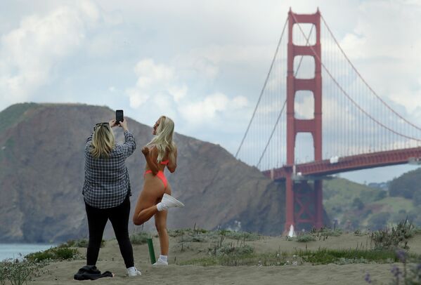 Женщина в бикини фотографируется на пляже Бейкер возле моста Золотые Ворота в США. - Sputnik Таджикистан