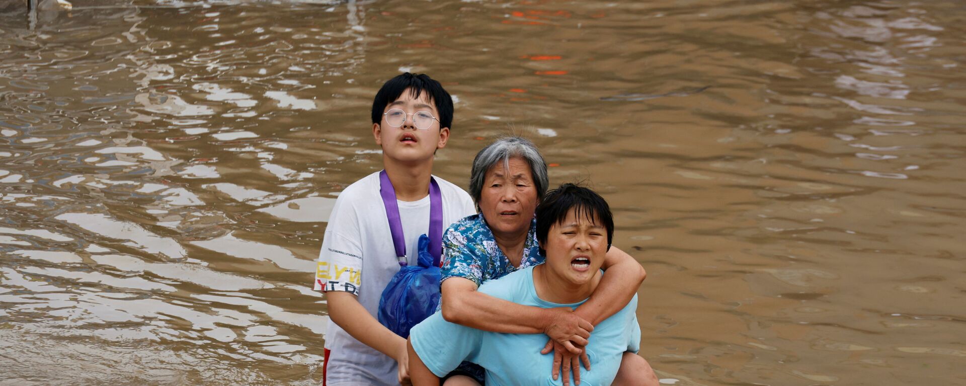 Женщина несет пожилую женщину  через паводковые воды после проливного дождя в Чжэнчжоу, провинция Хэнань, Китай - Sputnik Таджикистан, 1920, 26.07.2021