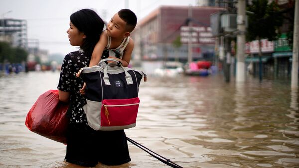 Женщина с ребенком и вещами пробирается через паводковые воды после проливного дождя в Чжэнчжоу, провинция Хэнань, Китай - Sputnik Тоҷикистон