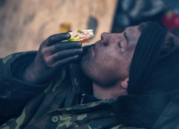 Участник акции оппозиции ест бутерброд на баррикаде на улице Грушевского в Киеве - Sputnik Таджикистан