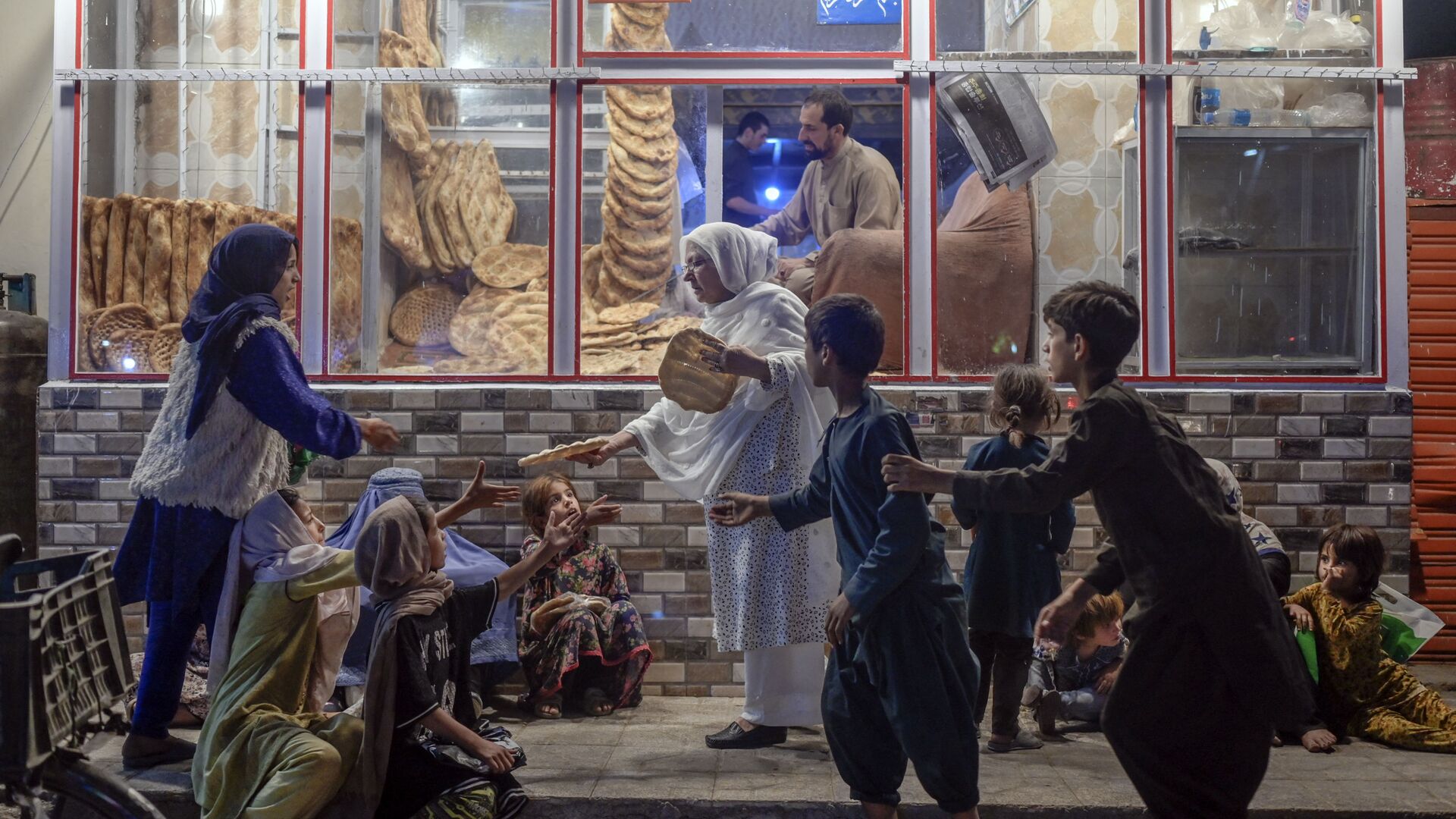 Женщина раздает хлеб нуждающимся детям перед пекарней в Кабуле - Sputnik Тоҷикистон, 1920, 06.12.2021