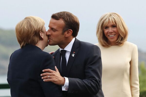Президент Франции Эммануэль Макрон приветствует канцлера Германии Ангелу Меркель поцелуем при своей жене Брижит Макрон. - Sputnik Таджикистан