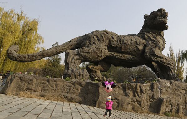 Девочка с шариком в форме Минни Маус на фоне скульптуры тигра в зоопарке Пекина. - Sputnik Таджикистан