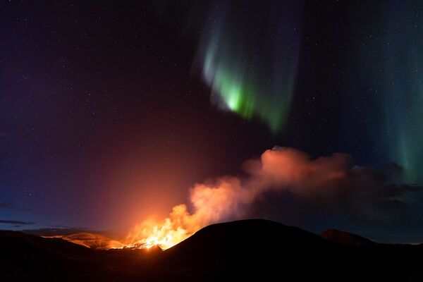 Северное сияние на фоне дыма от извергающегося вулкана Гелдингадалир на западе Исландии. - Sputnik Таджикистан