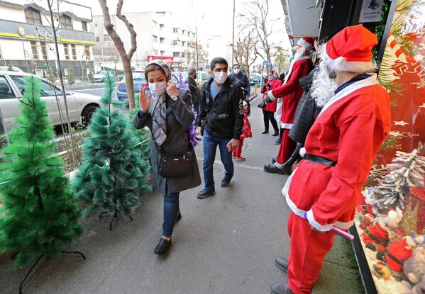 Мужчина в костюме Санты приветствует иранцев, проходящих мимо магазина рождественских украшений в Тегеране. - Sputnik Таджикистан