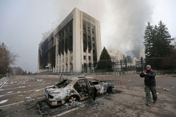 Очевидец фотографирует сгоревшую машину перед зданием мэрии - последствия общественных беспорядков из-за роста цен на топливо в Алматы. - Sputnik Таджикистан
