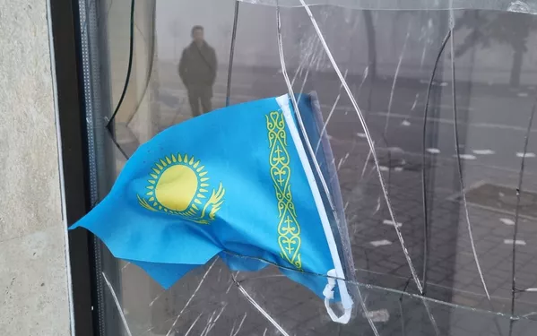 Парчами миллии Қазоқистон дар пасманзари тирезаи шикастаи филиали бонки маҳаллӣ ба нишони эътироз. Парчами миллии Қазоқистон дар пасманзари тирезаи шикастаи филиали бонки маҳаллӣ ба нишони эътироз. - Sputnik Тоҷикистон