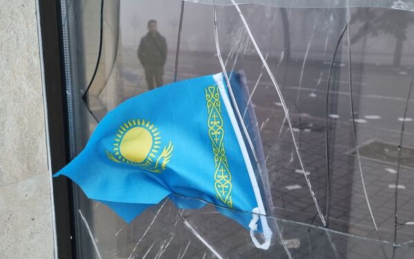 Государственный флаг Казахстана на фоне разбитого в знак протеста окна отделения местного банка. - Sputnik Таджикистан