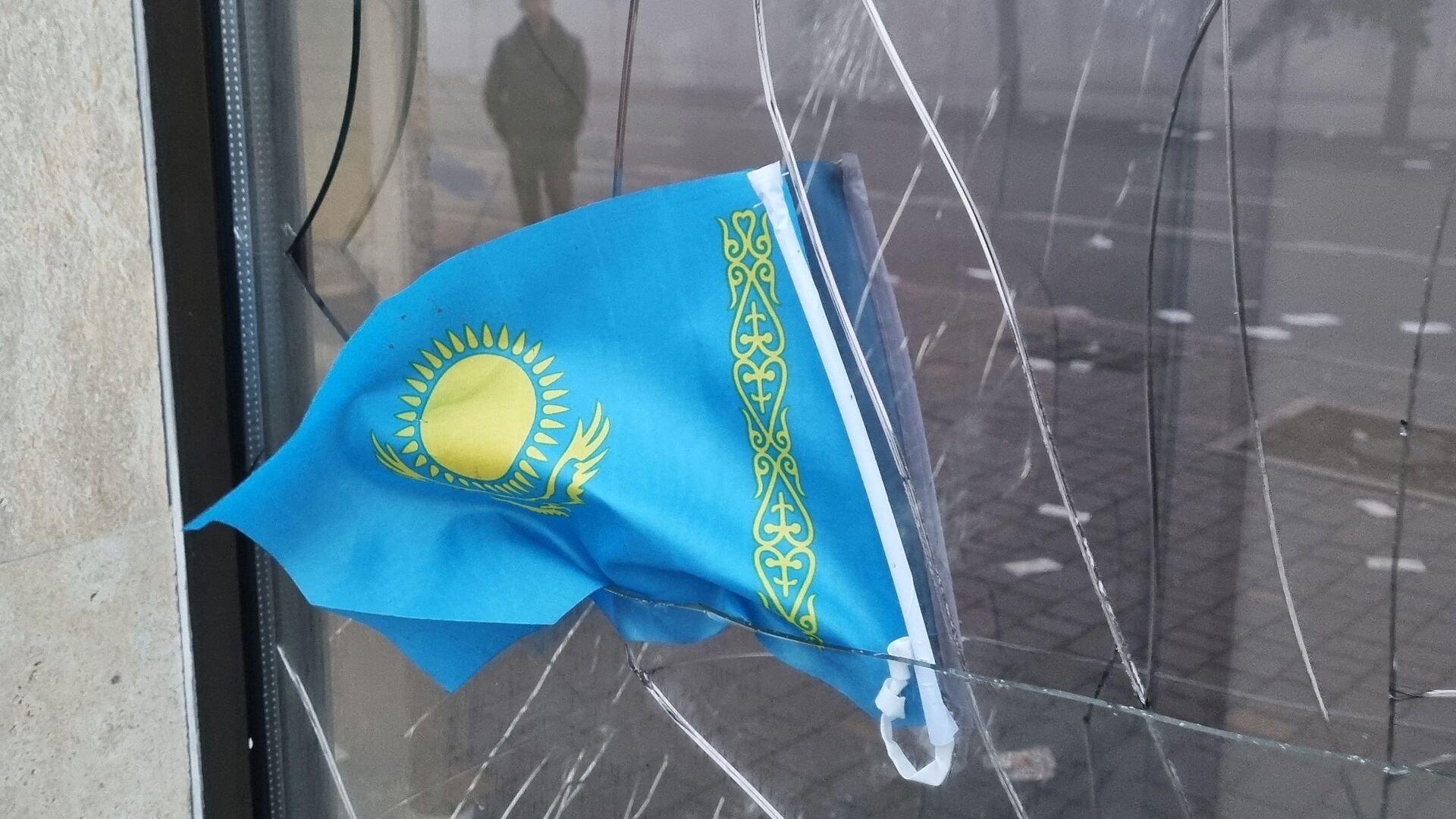 Государственный флаг Казахстана виден в разбитом окне отделения Kaspi Bank после протестов, вызванных повышением цен на топливо в Алматы - Sputnik Таджикистан, 1920, 08.01.2022