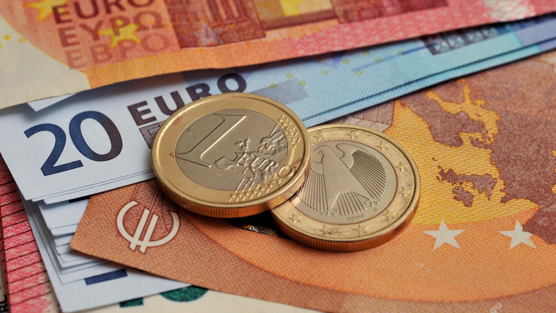 Монеты номиналом 1 евро на фоне банкнот номиналом 10 и 20 евро.  - Sputnik Таджикистан, 1920, 23.11.2022