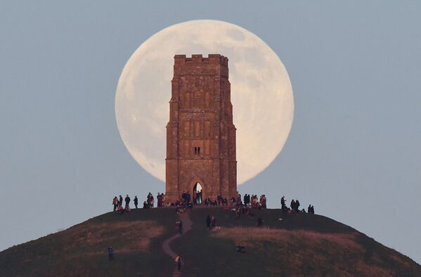 Люди стоят рядом с Башней Святого Михаила, наблюдая, как Волчья луна восходит за Гластонбери-Тор (Великобритания). - Sputnik Таджикистан