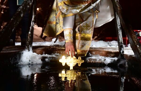 Перед входом людей в воду священнослужитель традиционно окунает распятие в купель. - Sputnik Таджикистан