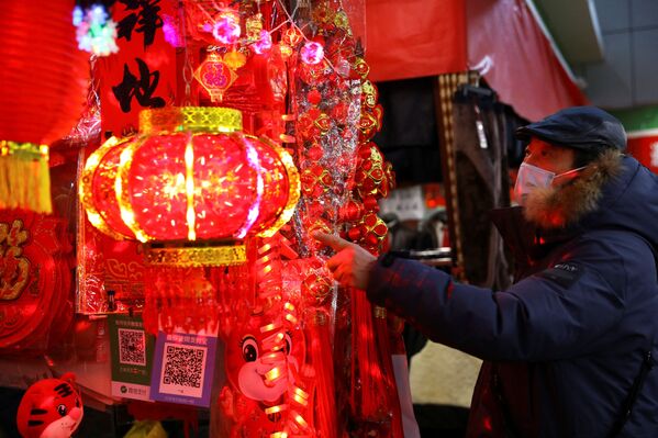 Покупатель выбирает украшения для китайского лунного Нового года, выставленные на прилавке на утреннем рынке в Пекине. - Sputnik Таджикистан