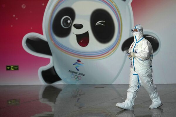 Медицинский сотрудник в защитном костюме в аэропорту Шоуду на фоне талисмана игра панды Бин Дунь Дунь. - Sputnik Таджикистан