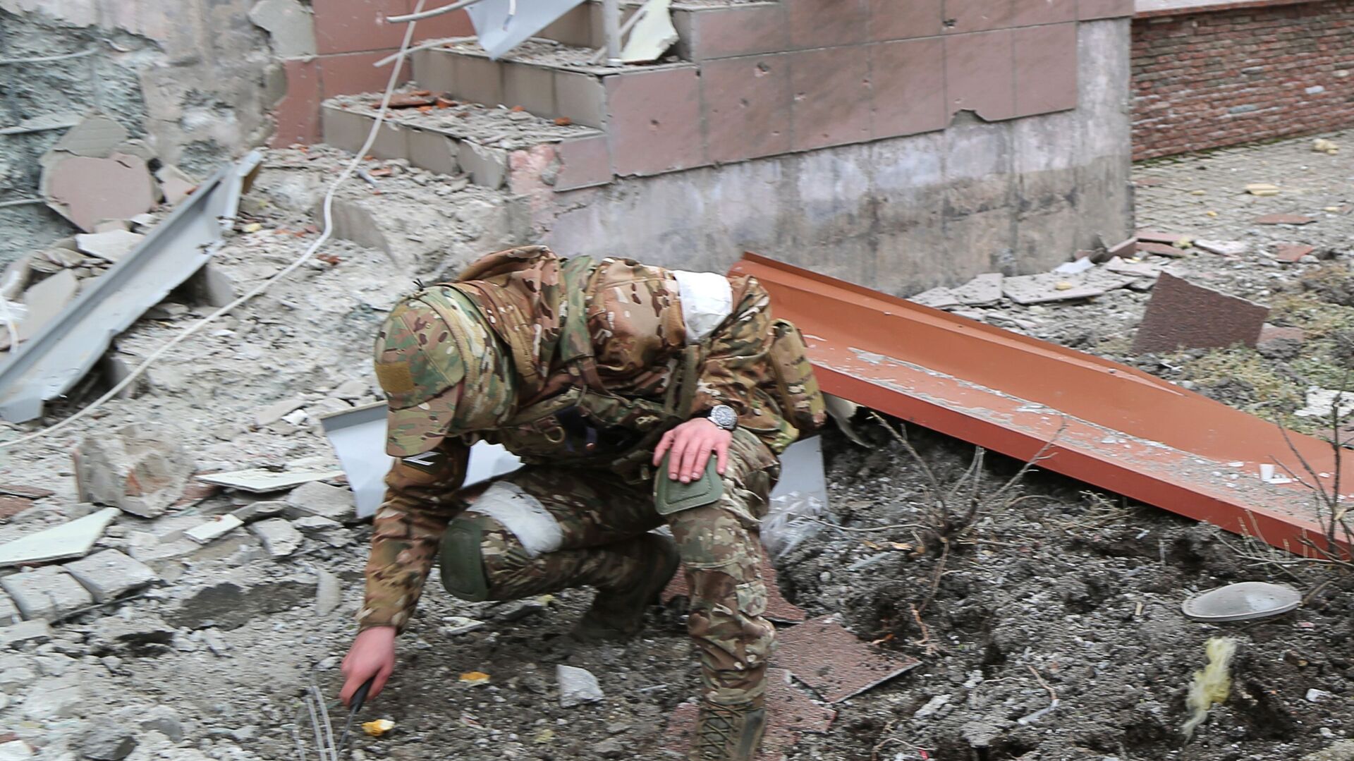Военнослужащий обследует воронку от взрыва во дворе многоэтажного жилого дома в Донецке, поврежденного в результате обстрела - Sputnik Таджикистан, 1920, 01.03.2022
