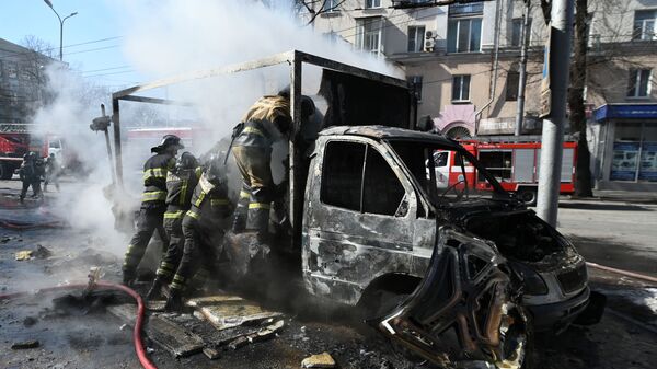 Сотрудники пожарной охраны у разрушенной машины в результате взрыва в центре Донецка - Sputnik Таджикистан