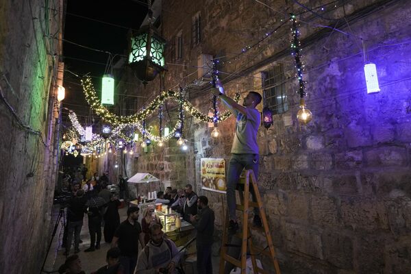 Палестинец вешает декоративные светильники в рамках подготовки к священному для мусульман месяцу Рамадан на улицах Старого Иерусалима. - Sputnik Таджикистан