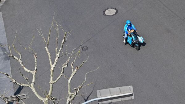 Работник службы доставки едет на скутере по улице, чтобы доставить товары жителям во время второго этапа карантина из-за Covid-19 в Шанхае - Sputnik Тоҷикистон