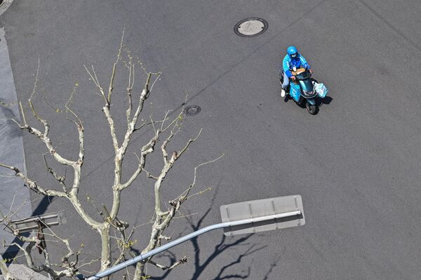 Работник службы доставки едет по безлюдной улице Шанхая на скутере. - Sputnik Таджикистан