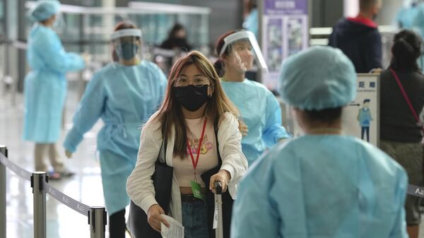 Рабочие в защитных костюмах направляют пассажиров к автобусам в карантинные отели в аэропорту Гонконга - Sputnik Таджикистан