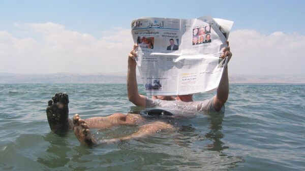 Человек лежит с газетой на поверхности Мёртвого моря, самого соленого водоема на Земле - Sputnik Таджикистан