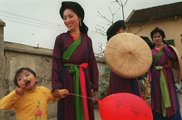 Девочка ест фруктовый лед рядом с исполнителями &quot;куан хо&quot; в традиционных костюмах в северной провинции Бакнинь, Вьетнам.  - Sputnik Таджикистан