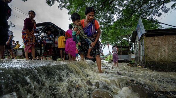 Женщина с ребенком на руках дорогу во время наводнения в деревне Корора (17 июня 2022). Индия - Sputnik Тоҷикистон