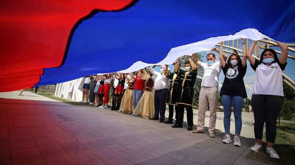 Участники празднований Дня России держат российский флаг в парке Дружбы города Георгиевска Ставропольского края - Sputnik Таджикистан
