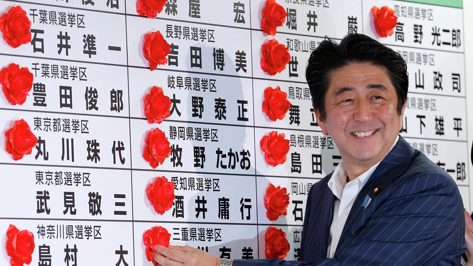 Премьер-министр Японии Синдзо Абэ ставит розетку на имя победившего кандидата от своей Либерально-демократической партии во время подсчета голосов на выборах в верхнюю палату парламента в штаб-квартире партии в Токио - Sputnik Таджикистан, 1920, 10.07.2022