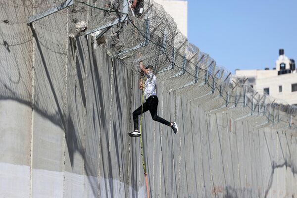 Юноша спускается по веревке через бетонную стену израильского разделительного барьера в район Бейт-Ханина в Восточном Иерусалиме. - Sputnik Таджикистан