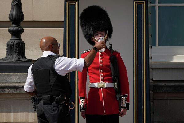 Полицейский поит британского солдата в традиционной медвежьей шапке, дежурящего у Букингемского дворца, в жаркую погоду в Лондоне. - Sputnik Таджикистан