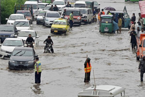 Пассажиры пробираются по затопленной улице после сильного ливня в Пешаваре, 17 августа 2022 года. - Sputnik Таджикистан