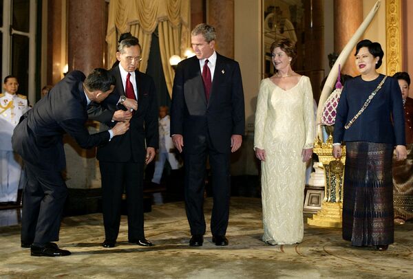 Президент США Джордж Буш-младший, первая леди Лора Буш и королева Таиланда Сирикит наблюдают, как королю Пхумипону поправляют галстук в Королевской галерее в Большом дворце, Бангкок, 19 октября 2003 года. - Sputnik Таджикистан