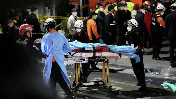 Спасатели несут пострадавшего на улице рядом с местом происшествия в Сеуле, где произошла давка
 - Sputnik Таджикистан