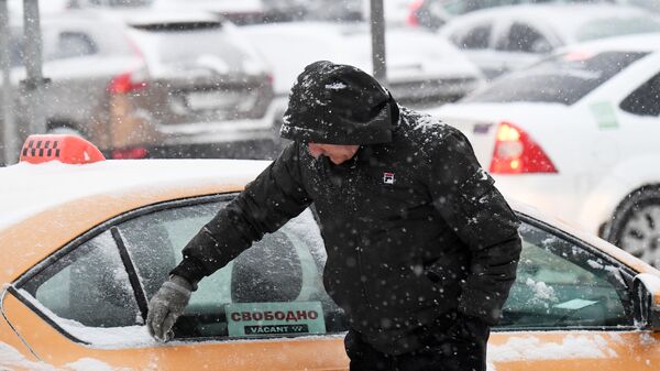 Водитель такси очищает автомобиль во время снегопада - Sputnik Таджикистан