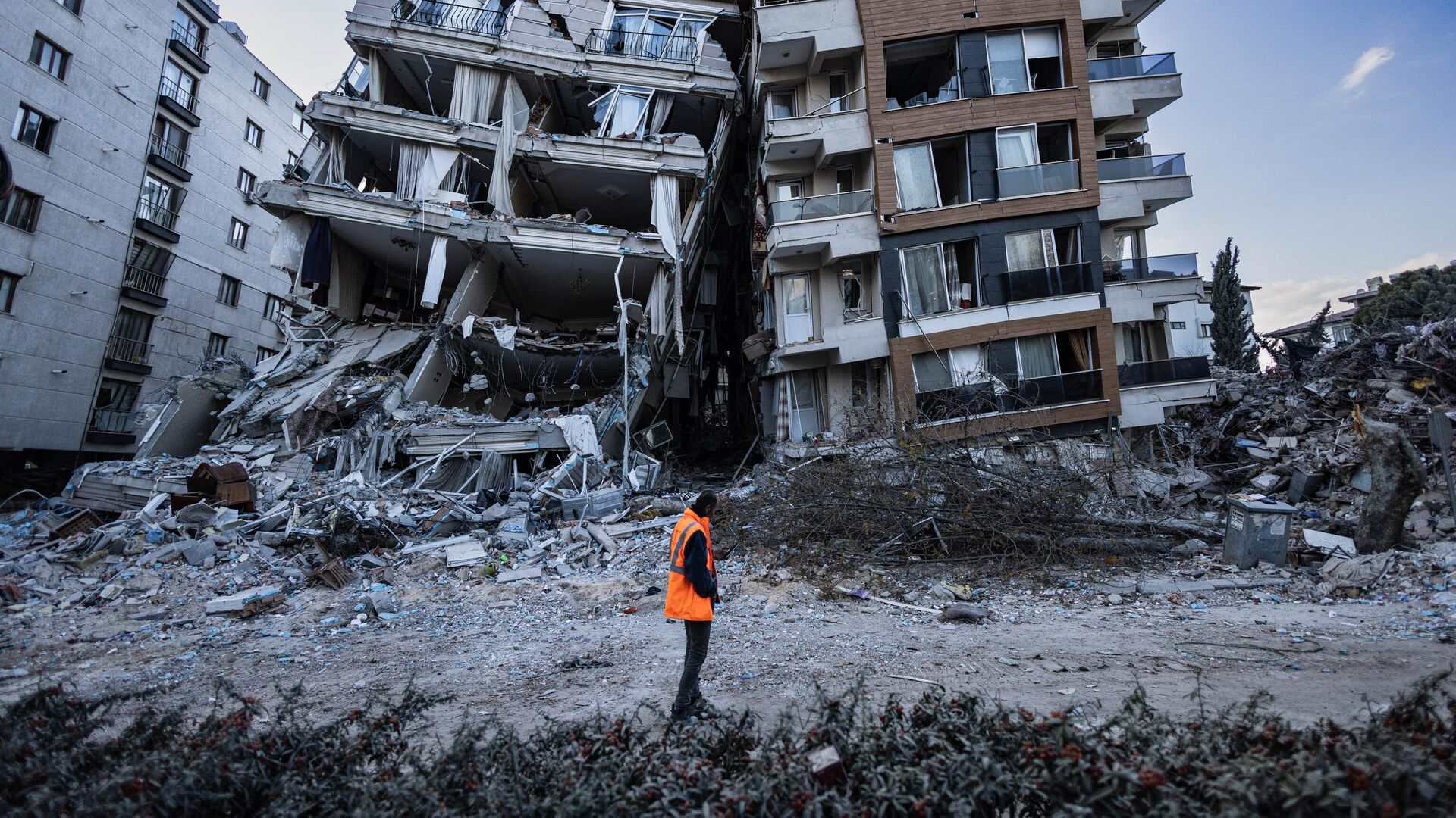 Спасатель проходит мимо частично разрушенных в результате землетрясений зданий в городе Антакья, Турция - Sputnik Таджикистан, 1920, 19.03.2023