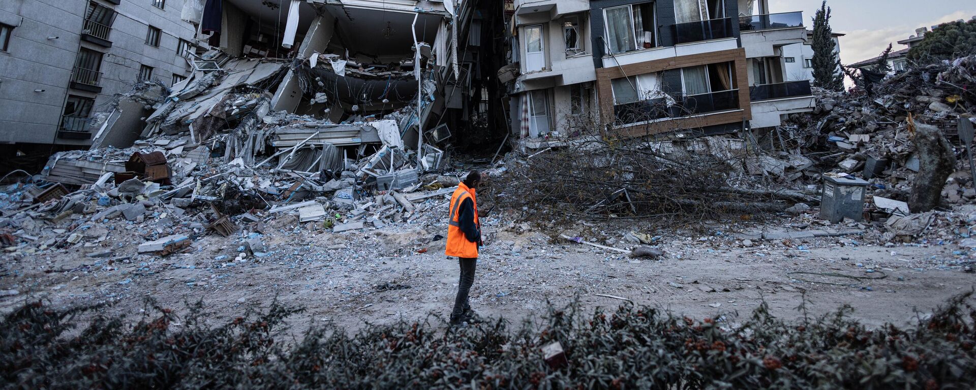 Спасатель проходит мимо частично разрушенных в результате землетрясений зданий в городе Антакья, Турция - Sputnik Тоҷикистон, 1920, 26.02.2023