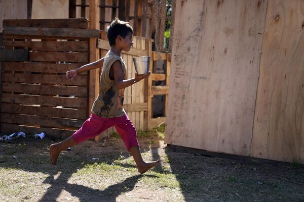 Ребенок бежит с контейнером, наполненным водой, на территории своего временного приюта в Асунсьоне, Парагвай. - Sputnik Таджикистан