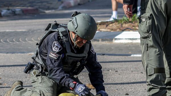 Сотрудник подразделения израильской полиции по обезвреживанию бомб осматривает остатки снаряда, Израиль - Sputnik Таджикистан