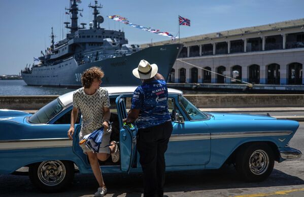 Турист выходит из классического американского автомобиля перед учебным кораблем ВМФ России &quot;Перекоп&quot; в Гаванской бухте, Куба. - Sputnik Таджикистан