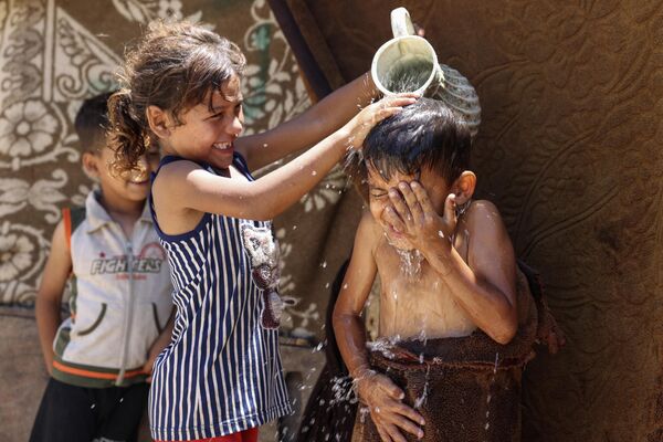 Девочка поливает мальчика водой из-за жары в городе Газа. - Sputnik Таджикистан
